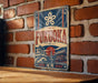 a vintage-style sign with the name "FUKUOKA" displayed prominently. The sign is mounted on a brick wall, and there is a wooden table in the foreground.