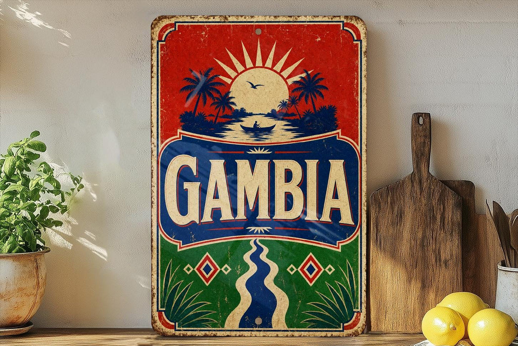 a vintage-style sign with the word "Gambia" prominently displayed, surrounded by tropical elements such as palm trees and a sun. The sign is placed on a wooden surface, with a potted plant and a wooden cutting board visible in the background.