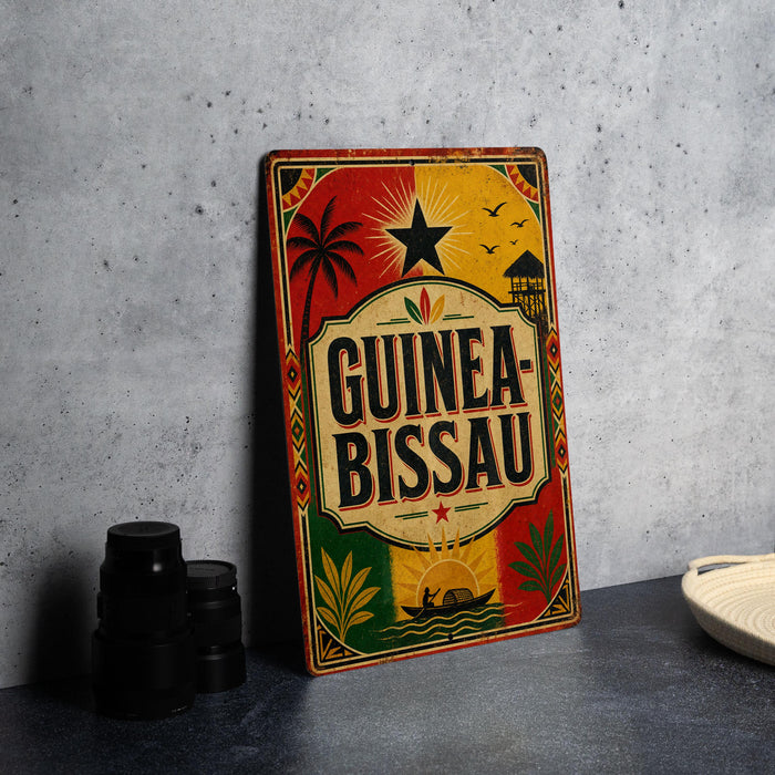 A colorful vintage-style sign for Guinea-Bissau, featuring a palm tree, sun, and other tropical elements, is displayed on a gray countertop next to a stack of black camera lenses.