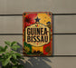 A colorful sign with the text "GUINEA-BISSAU" displayed prominently on a wall, with various decorative elements such as palm trees, a sun, and a boat.