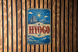 A vintage-style metal sign with the word "HYOGO" prominently displayed, featuring a castle, bridge, and sun in the background.