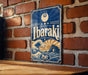 A vintage-style metal sign with the word "Ibaraki" displayed prominently, featuring a wave and a sun design. The sign is mounted on a brick wall, and there is a wooden table below it.