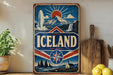 A vintage-style sign for Iceland, featuring a mountain landscape with a waterfall, a sun, and a red and blue border.