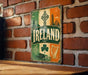 A vintage-style metal sign with the word "IRELAND" prominently displayed, featuring various Irish symbols and landmarks such as a harp, a shamrock, and a castle.