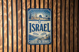 A vintage-style metal sign with the word "ISRAEL" prominently displayed, featuring a sunburst design and images of landmarks and architecture.