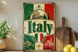 A vintage-style metal sign with the word "Italia" prominently displayed, featuring a collage of images related to Italy, such as landmarks, landscapes, and traditional Italian cuisine.