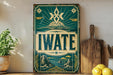 A vintage-style sign with the word "IWATE" prominently displayed, featuring a mountain landscape and a star design. The sign is mounted on a wall, and there are some kitchen utensils and a potted plant visible in the foreground.