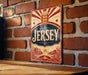 A vintage Jersey sign is displayed on a brick wall, featuring a red and gold design with a sunburst pattern and a coat of arms.