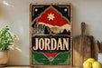 a vintage-style sign with the word "JORDAN" prominently displayed, along with a graphic of a building and mountains. The sign is placed on a shelf next to a wooden cutting board and a potted plant.