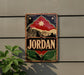 A vintage-style metal sign with the word "JORDAN" prominently displayed, featuring a decorative border and a star at the center. The sign is mounted on a gray wall, and there is a plant visible to the left of the sign.