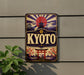 A vintage-style sign with the word "KYOTO" prominently displayed, featuring a sun and pagoda design, along with cherry blossom flowers and a temple.