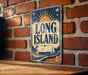 A vintage-style metal sign with the text "LONG ISLAND" and a lighthouse illustration is displayed on a brick wall.