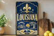 A vintage-style sign for Louisiana, featuring a fleur-de-lis symbol, a steamboat illustration, and a sunset scene.