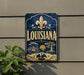 A vintage-style sign for Louisiana, featuring a fleur-de-lis symbol, a steamboat, and other nautical elements, mounted on a wall.