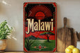 a vintage-style sign with the word "Malawi" prominently displayed, along with a sun and landscape design. The sign is placed on a shelf next to a wooden cutting board and a potted plant.