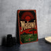 A vintage metal sign with the word "Malawi" on it, featuring a sun and landscape design, is displayed on a gray countertop next to some black camera lenses.