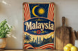 A vintage-style metal sign with the word "Malaysia" prominently displayed, featuring a crescent moon, sun, and a city skyline.