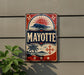 A vintage-style sign with the word "MAYOTTE" displayed prominently, featuring a sun and palm tree design.