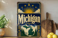 A vintage-style metal sign with the word "Michigan" prominently displayed, featuring a sun and clouds design, surrounded by a green maple tree silhouette.