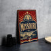 A vintage-style metal sign with the word "Missouri" prominently displayed, featuring a riverboat illustration and a starburst design.