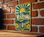 A vintage-style metal sign with a tropical beach scene and the word "Miyazaki" displayed on it, mounted on a brick wall.