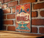A vintage-style metal sign with the word "Moorea" prominently displayed, featuring a sun and palm trees, is mounted on a brick wall.