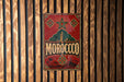 A vintage metal sign with the word "MOROCCO" displayed prominently in the center, surrounded by decorative elements such as a star and floral patterns.