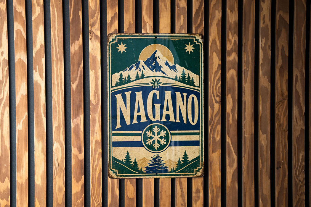 A vintage metal sign with the word "NAGANO" displayed prominently in the center, surrounded by a mountain landscape and snowflake design.