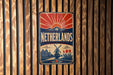 A vintage-style metal sign with the word "Netherlands" prominently displayed, featuring a sunburst design and a windmill illustration.