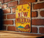 A vintage-style metal sign with the text "NEW MEXICO" is displayed on a brick wall, featuring a desert landscape and sun motif.