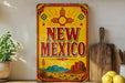 A vintage-style sign for New Mexico, featuring a desert landscape with mountains and a sun design, is displayed on a shelf next to a wooden cutting board and some kitchen utensils.
