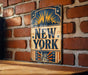 A vintage-style metal sign with the text "NEW YORK" prominently displayed, featuring a stylized depiction of the Statue of Liberty.