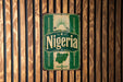 A vintage-style metal sign with the word "Nigeria" prominently displayed, featuring a map of Nigeria and decorative elements.