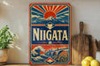 A vintage-style sign with a sun and mountain design, featuring the word "NIGATA" prominently displayed. The sign is placed on a shelf next to a wooden cutting board and some potted plants.