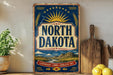A vintage-style sign for North Dakota, featuring a sun and wheat design, is displayed on a shelf next to a wooden cutting board and some lemons.