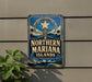 A vintage-style sign for the Northern Mariana Islands, featuring a star and palm trees, is displayed on a wall next to a plant.