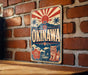 A vintage-style sign for "OKINAWA" is displayed on a brick wall, featuring a sun and palm trees, a lion, and a hibiscus flower.