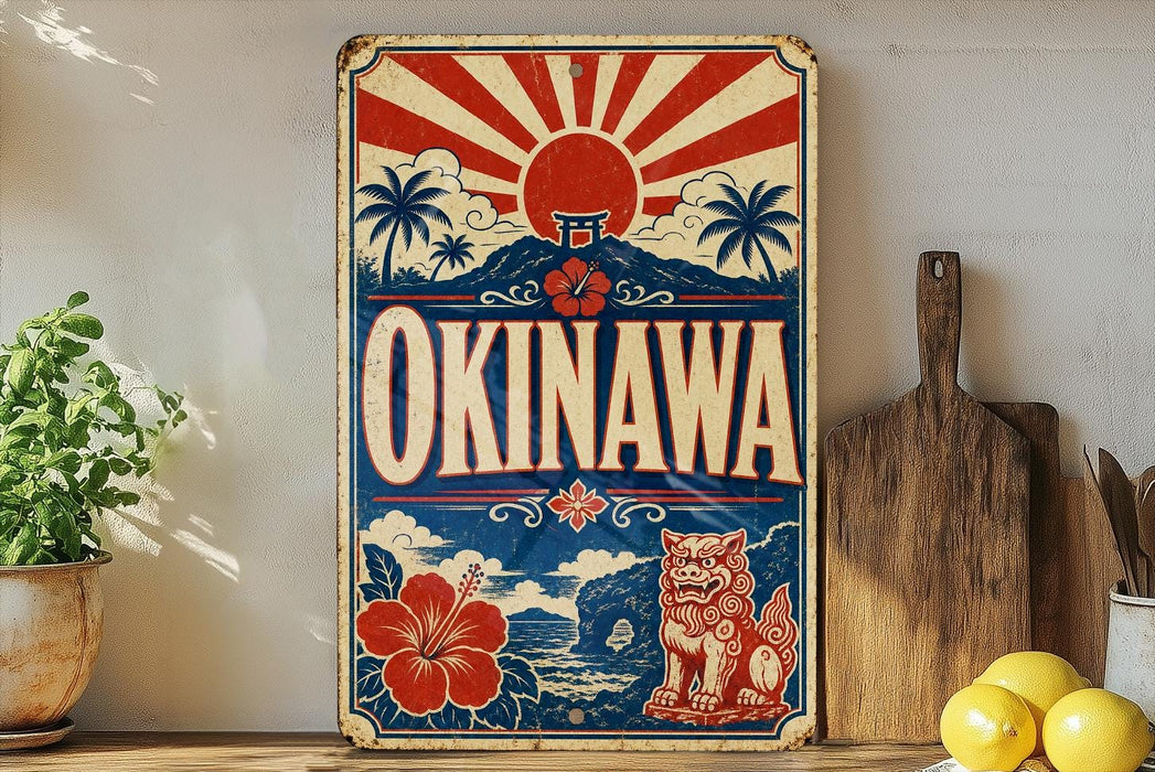 A vintage-style metal sign with the text "OKINAWA" prominently displayed, featuring a red and white sunburst design, a Japanese-style torii gate, and a red and white lion. The sign is placed on a wooden surface, with a potted plant, a wooden cutting board, and some lemons nearby.