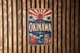 A vintage-style sign for the city of Okinawa, featuring a red and white sun design and a Japanese-style lion.