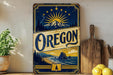 A vintage-style sign for Oregon featuring a mountain landscape with a sun and stars, along with the state's name in a decorative font.