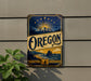 A vintage-style sign for Oregon, featuring a mountain landscape with a sun and stars, is displayed on a wall next to a plant.