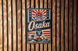 a vintage-style metal sign with the word "Osaka" prominently displayed, along with a wave and a castle-like structure.