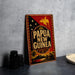 A vintage metal sign with the text "Papua New Guinea" and a decorative border, featuring a bird and a tropical landscape, is displayed on a gray surface.