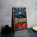 A vintage metal sign with a colorful design, featuring a sun, palm trees, mountains, and the word "Reunion" prominently displayed.