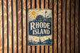 A vintage-style metal sign with the text "RHODE ISLAND" and a lighthouse illustration is displayed on a wooden wall.