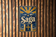 A vintage-style sign with the word "Saga" displayed prominently in the center, surrounded by a sunburst design and a cross.