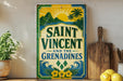 A vintage-style sign for Saint Vincent and the Grenadines, featuring a tropical landscape with palm trees and a sun. The sign is displayed on a shelf next to a wooden cutting board and a potted plant.