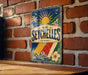A vintage-style metal sign with the word "SEYCHELLES" displayed prominently, featuring a tropical landscape with palm trees, a sun, and a hibiscus flower.
