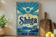 a vintage Shiga sign with a blue and white color scheme, depicting a scenic landscape with mountains and a temple. The sign is placed on a shelf next to a wooden cutting board and a potted plant.