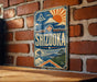 A vintage-style sign for Shizuka, a city in Japan, is displayed on a brick wall.
